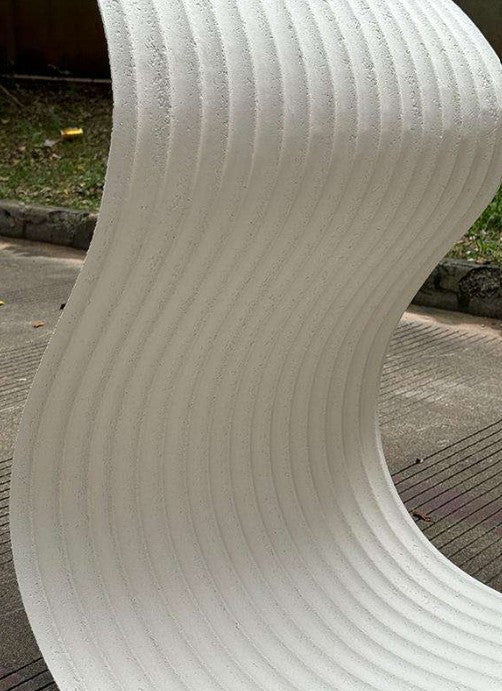 Curved white3D RIPPLE FLEXIBLE NATURAL STONE BOARD texture on a blurred outdoor background